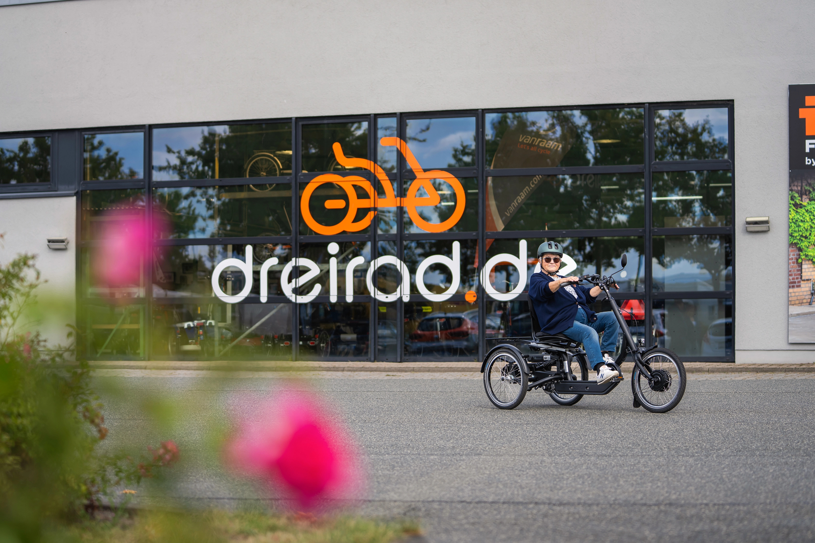 Frau fährt mit Dreirad vor einem Laden wo das dreirad.de Logo an der Scheibe zu sehen ist