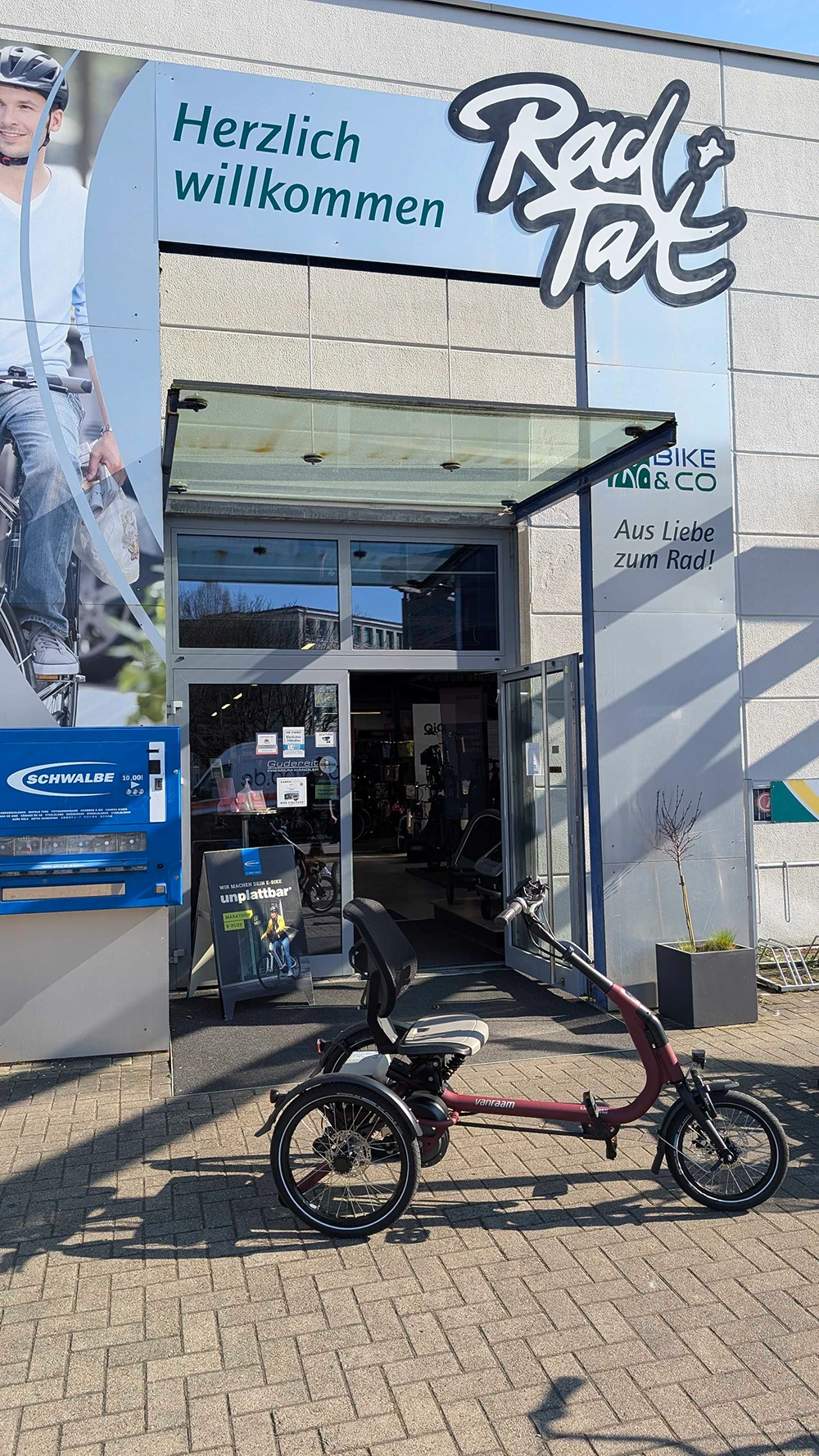 Van Raam Dreirad vor dem Fahrradgeschäft RadTat mit offenem Eingang und Begrüßungsschild.