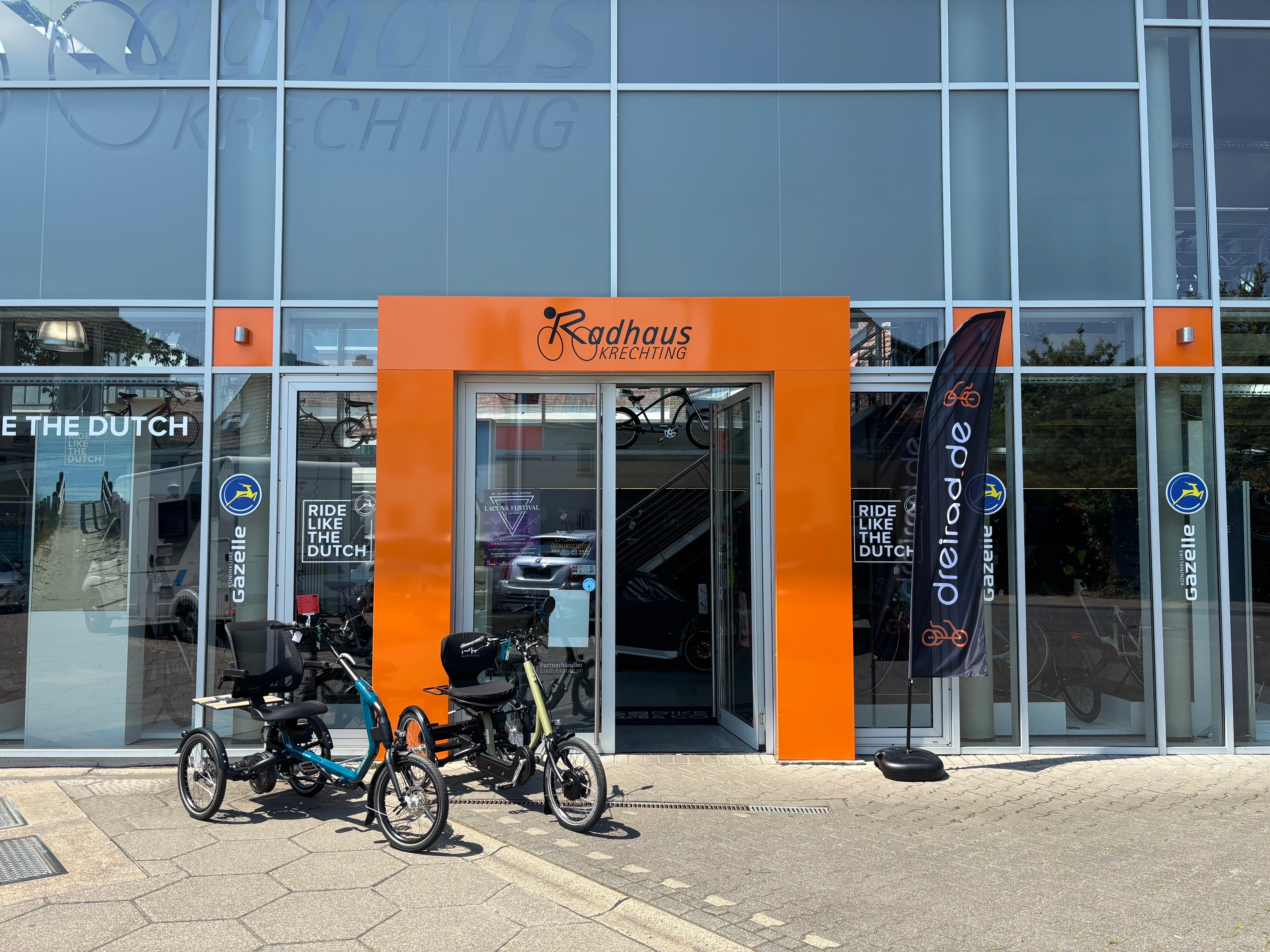 Eingang Fahrradladen und davor stehen zwei Dreiräder und eine Fahne mit Aufdruck dreiradde