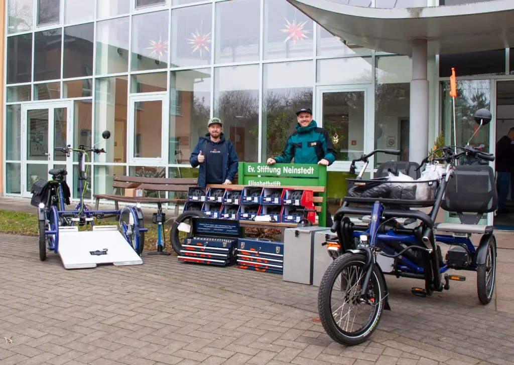 Personen stehen mit Therapiefahrräder vor einem Gebaeude