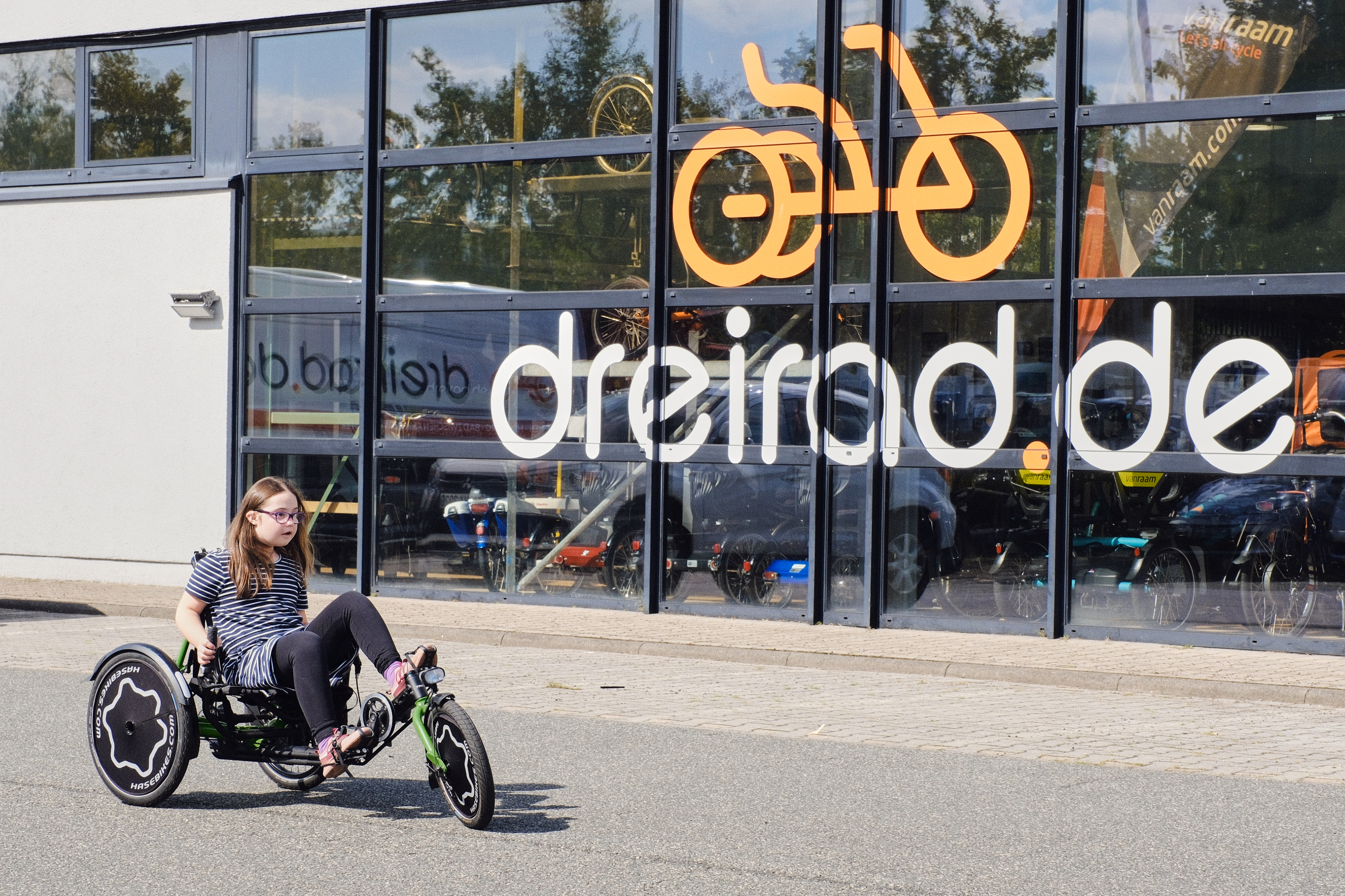 Kind fährt ein Liegedreirad vor dreirad.de Filiale