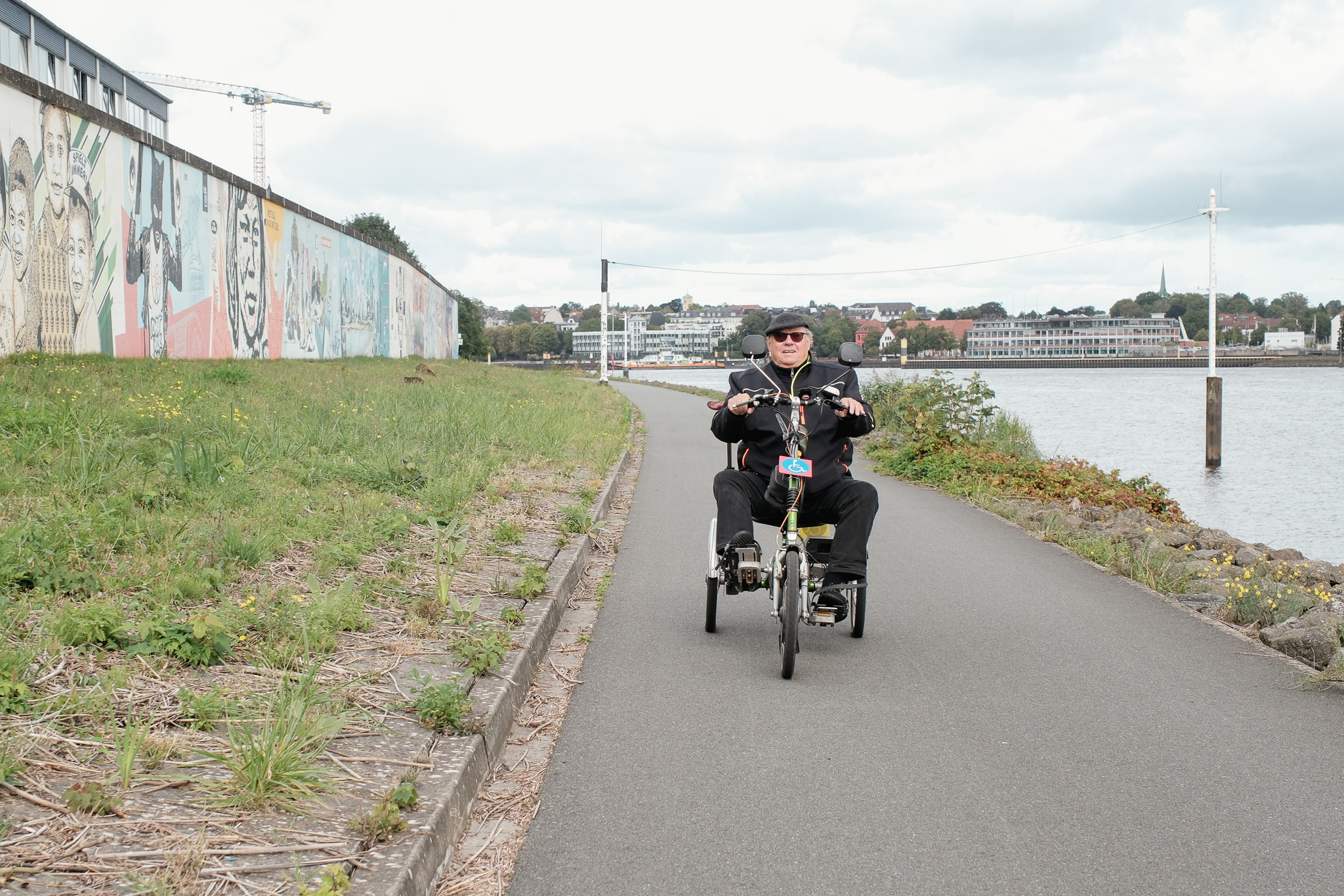 Mann fährt mit einem Dreirad auf dem Radweg neben einem Fluss