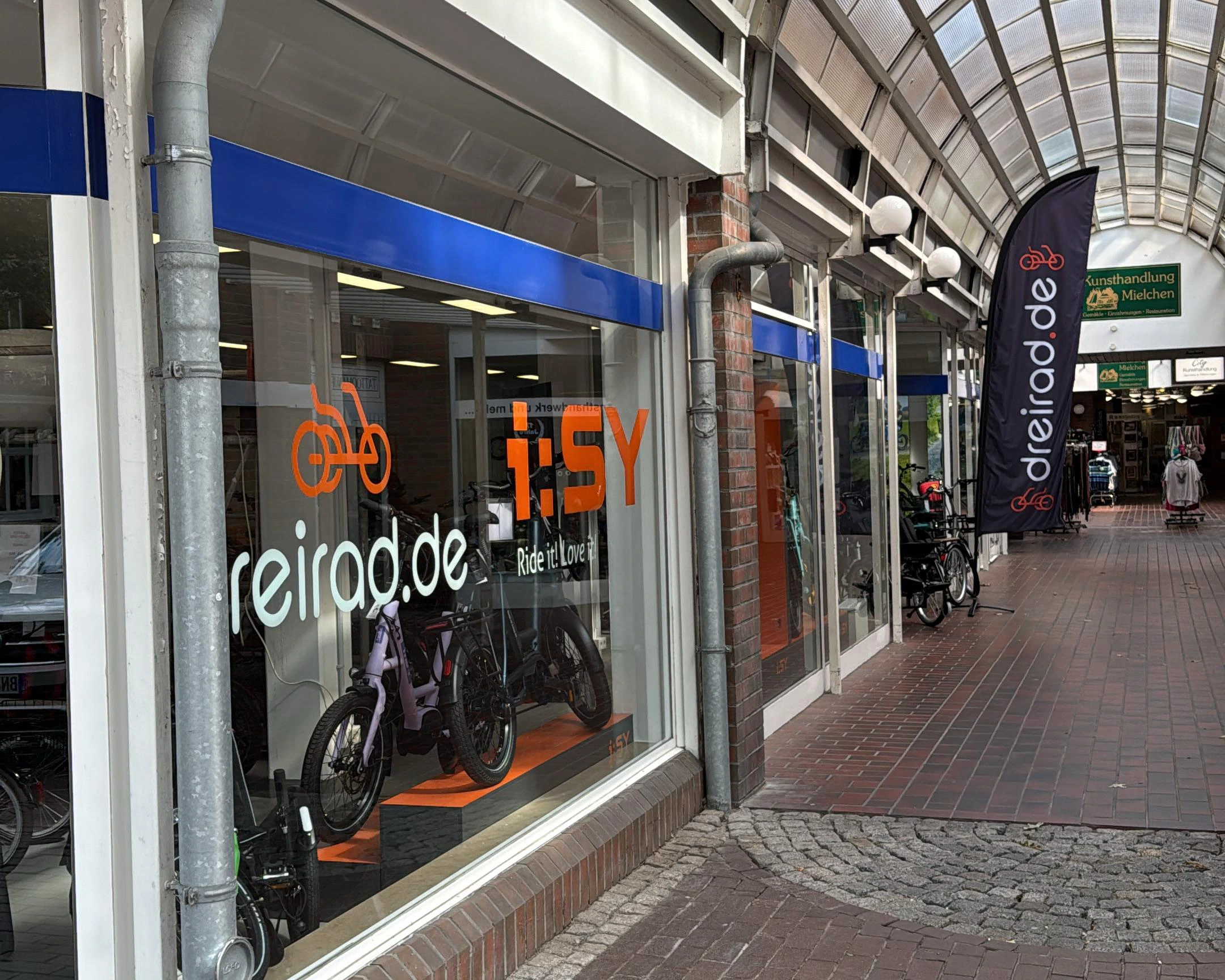 Schaufenster mit Aufschrift dreirad.de und Beachflag vor dem Laden