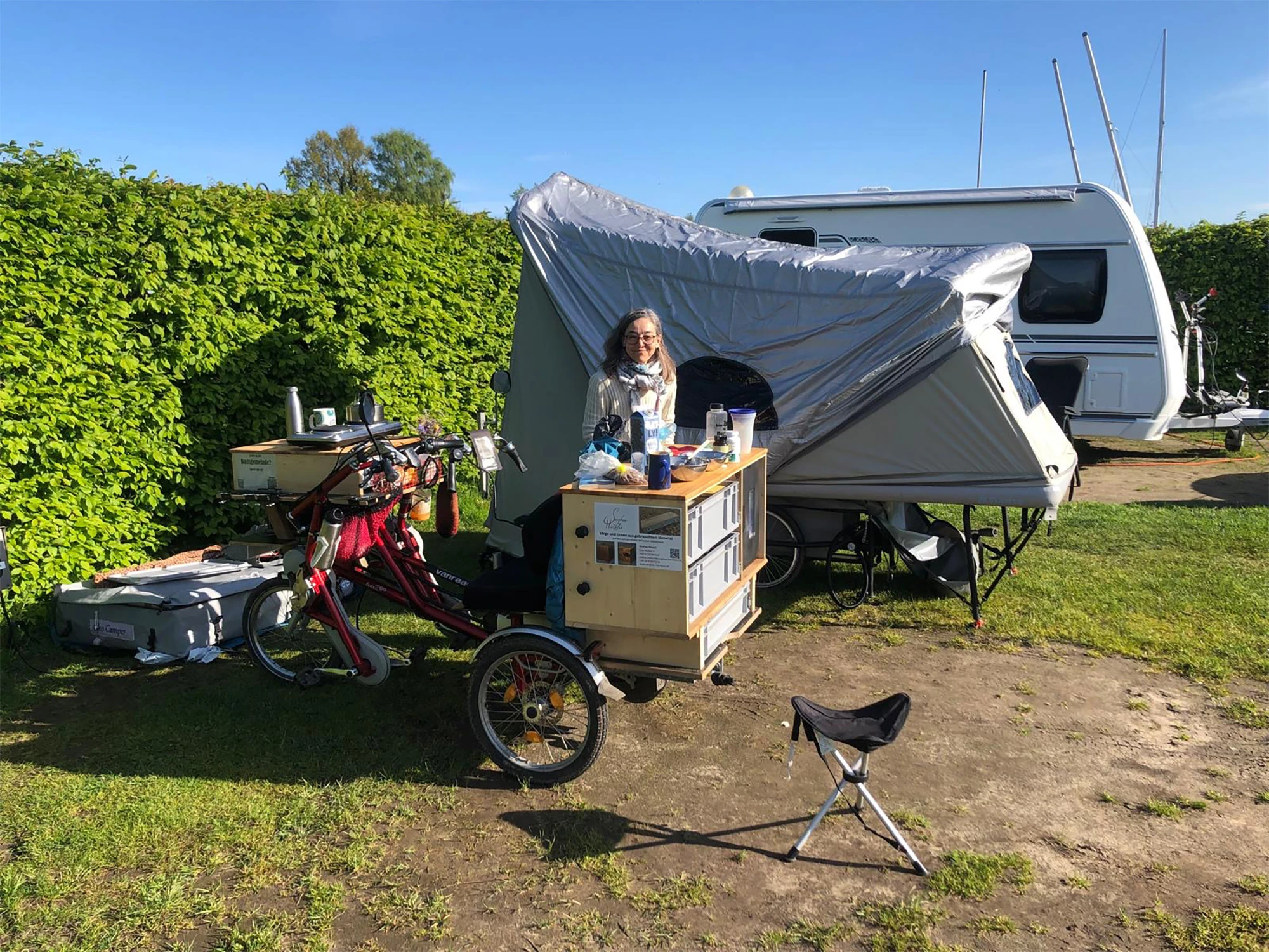  frau steht vor dreirad mit küche und aufgebautem vorzelt am wohnwagen auf campingplatz